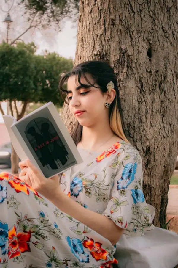 A woman reading a book while sitting on a park bench